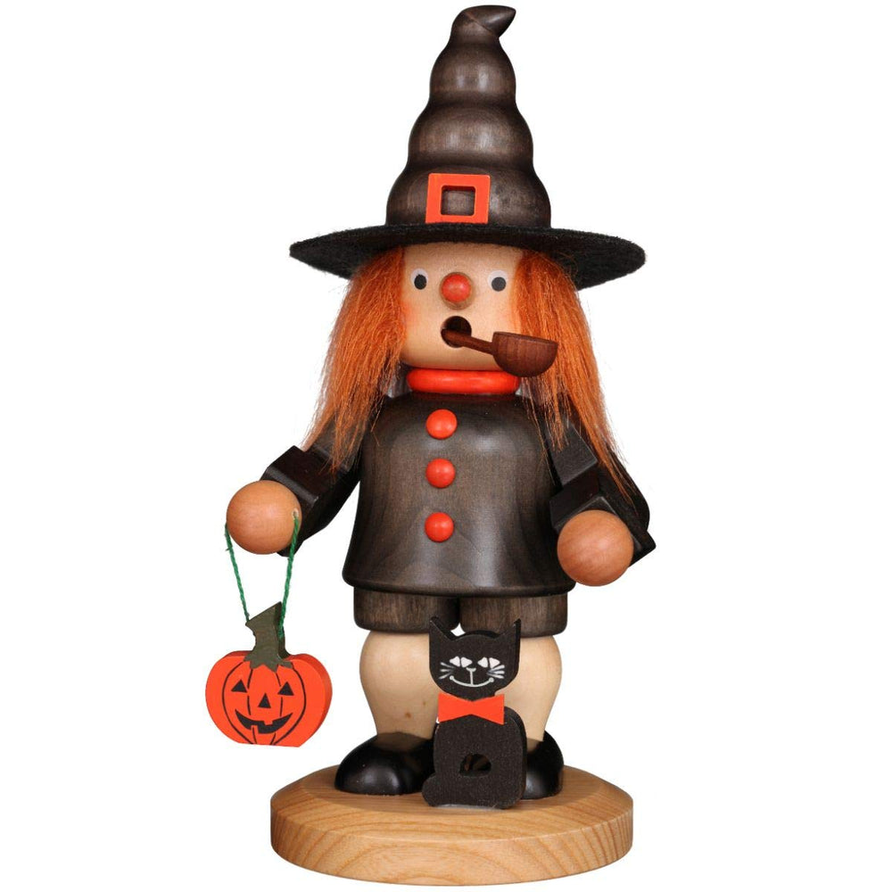 A wooden witch figurine holding a cat, with a pumpkin at her feet, showcasing a whimsical Halloween theme.