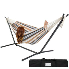 A woman sits comfortably in a hammock, with a bag resting next to her, surrounded by a serene outdoor setting.