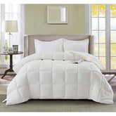 A white comforter and multiple pillows arranged on a bed, offering a soft and comfortable sleeping space.