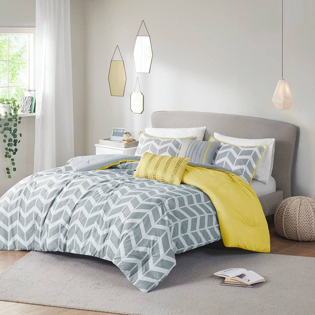 A stylish yellow and gray chevron comforter set draped over a bed, enhancing the room's contemporary aesthetic.