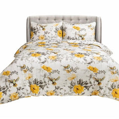 A bed featuring a yellow and gray floral comforter and a white pillow, creating a bright and inviting look.