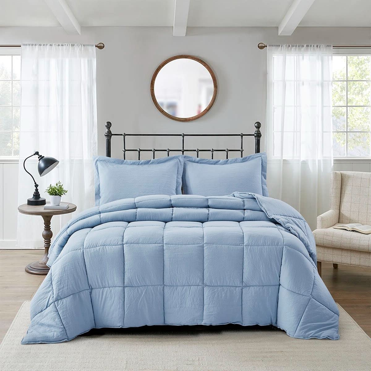 A blue comforter draped over a black frame, with decorative pillows placed at the head of the bed.