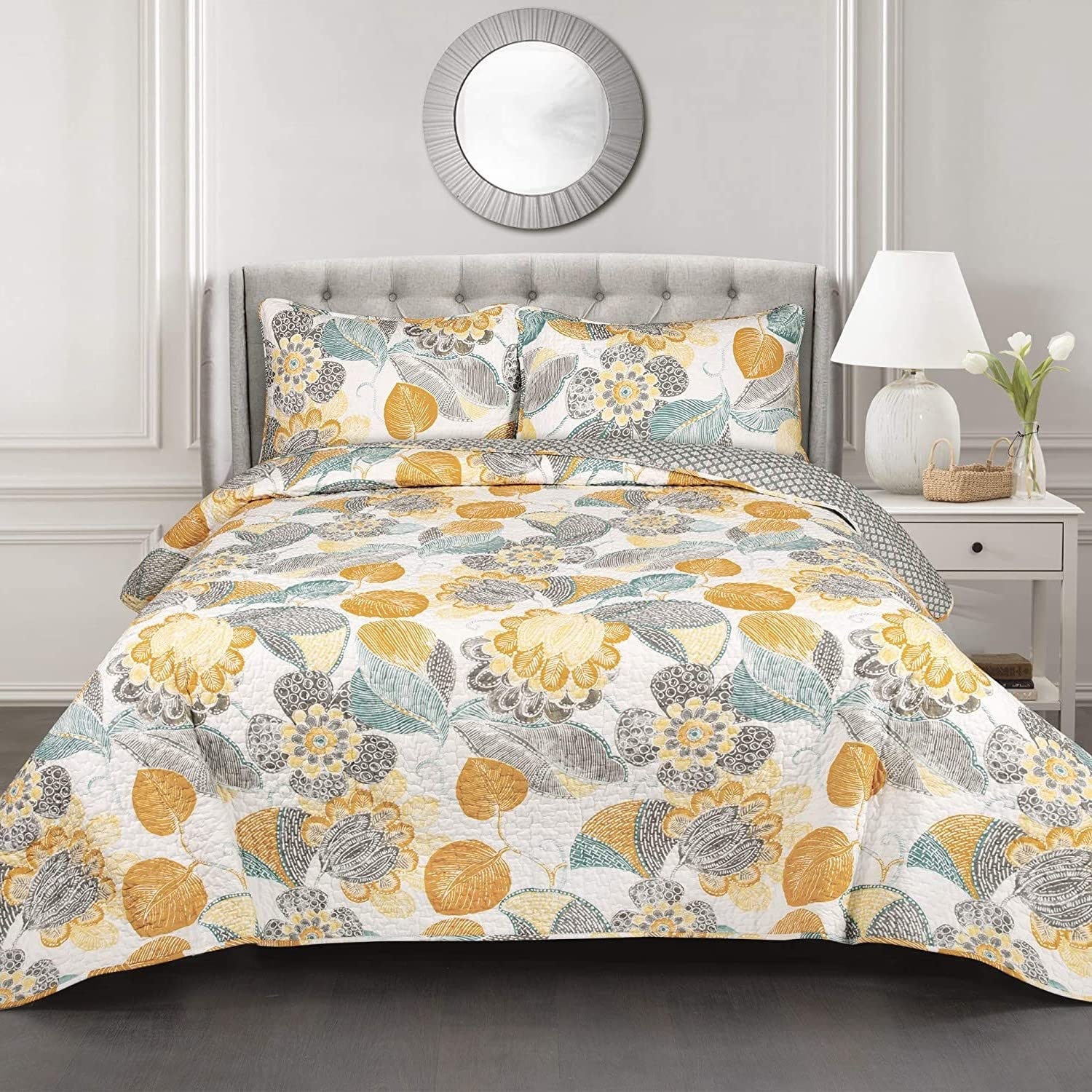 A floral bedspread in yellow and gray covers a bed, complemented by a sleek white headboard, enhancing the room's decor.