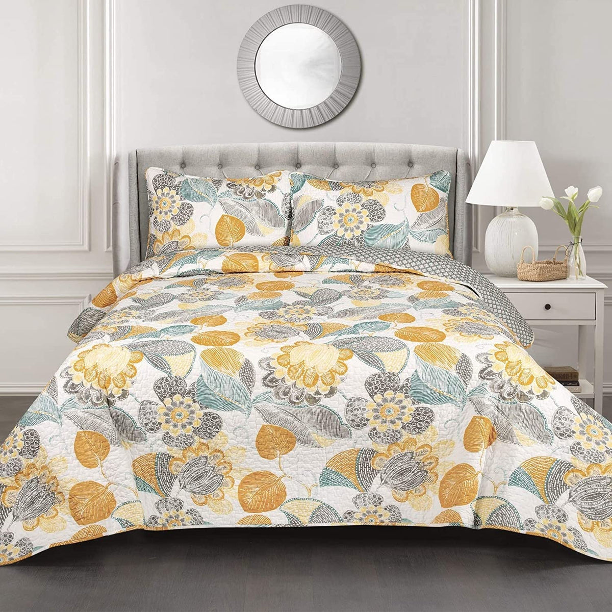 A floral bedspread in yellow and gray covers a bed, complemented by a sleek white headboard, enhancing the room's decor.