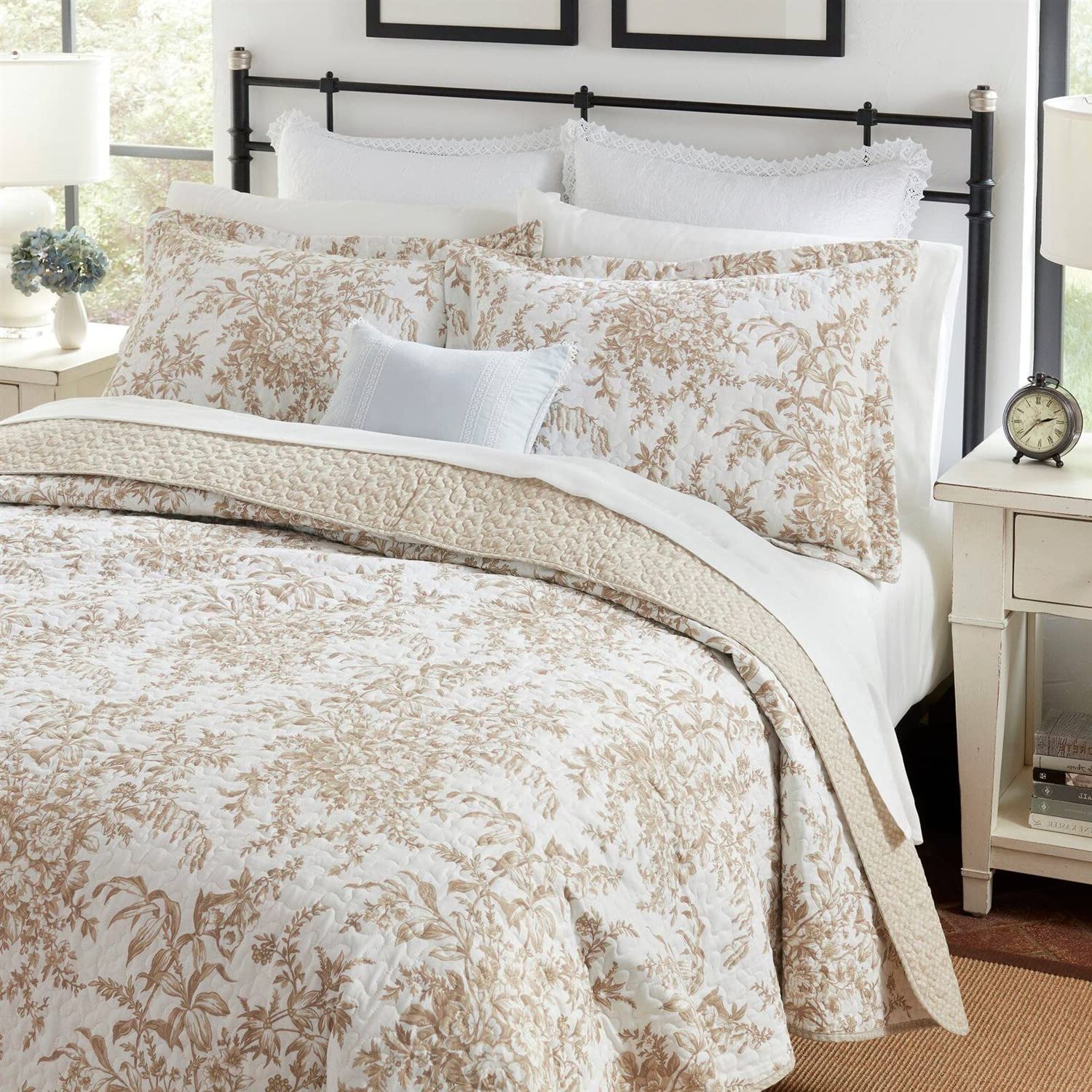 A white and beige comforter featuring a delicate floral pattern, elegantly draped on a bed.