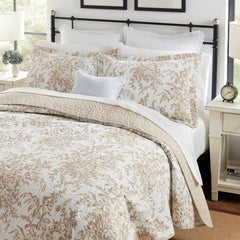 A white and beige comforter featuring a delicate floral pattern, elegantly draped on a bed.